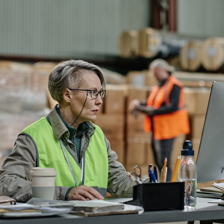 Worker sitting at her workplace in warehouse and working on computer